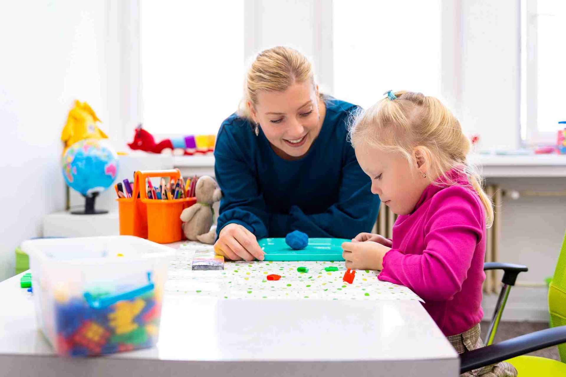 Two children painting at a white table in a bright classroom
