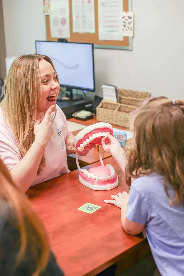 Woman showing mouth model to child in an office, with a computer and desk nearby
