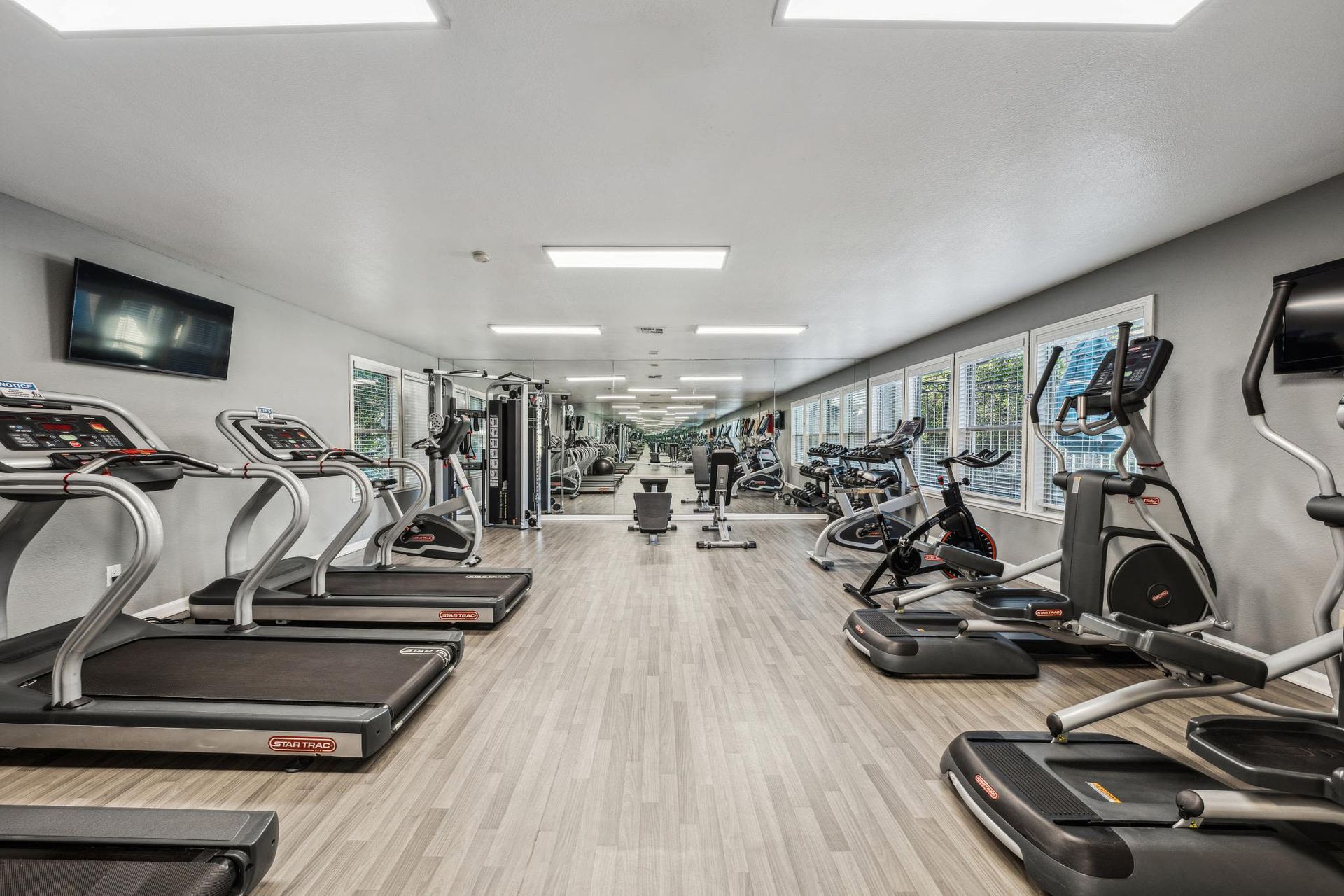 Well-lit fitness center with treadmills, bikes, and weight machines along large windows at Sterling Heights apartments in Benicia, CA.