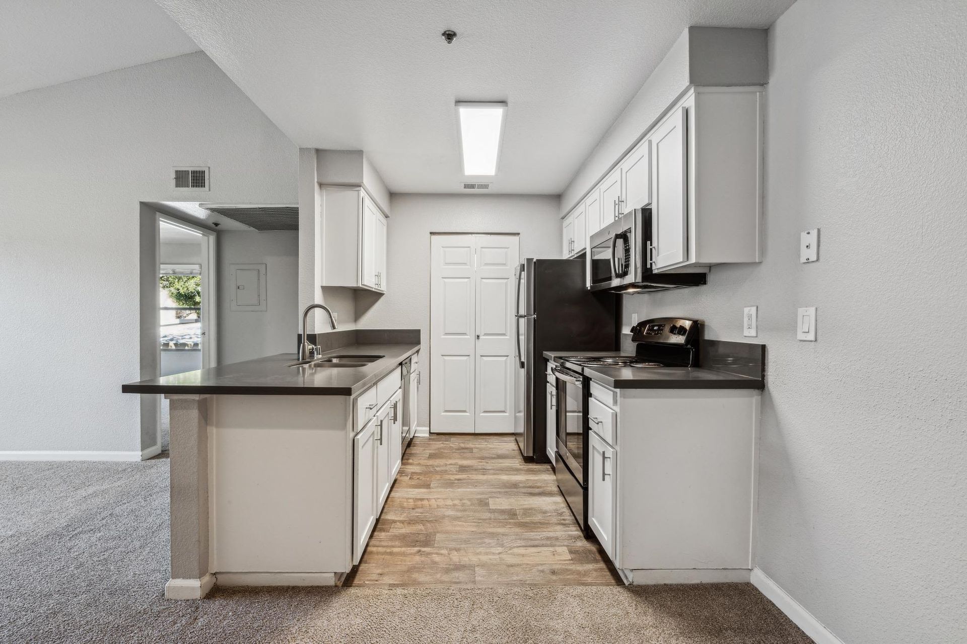 Interior apartment kitchen with white cabinets, dark countertops, an island, and stainless steel appliances at Sterling Heights apartments in Benicia, CA.