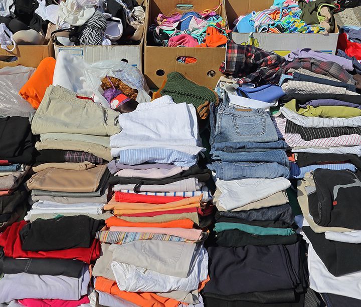 Stacks of folded clothes in various colors and patterns arranged on tables at an outdoor market.