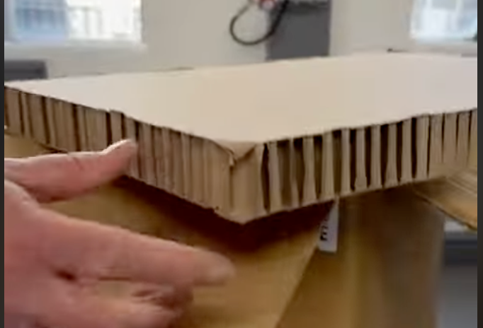 Hand holding a corrugated cardboard sample with a layered edge on a work surface