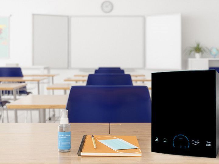 A classroom with tables , chairs , a notebook , a bottle of hand sanitizer and a air purifier.