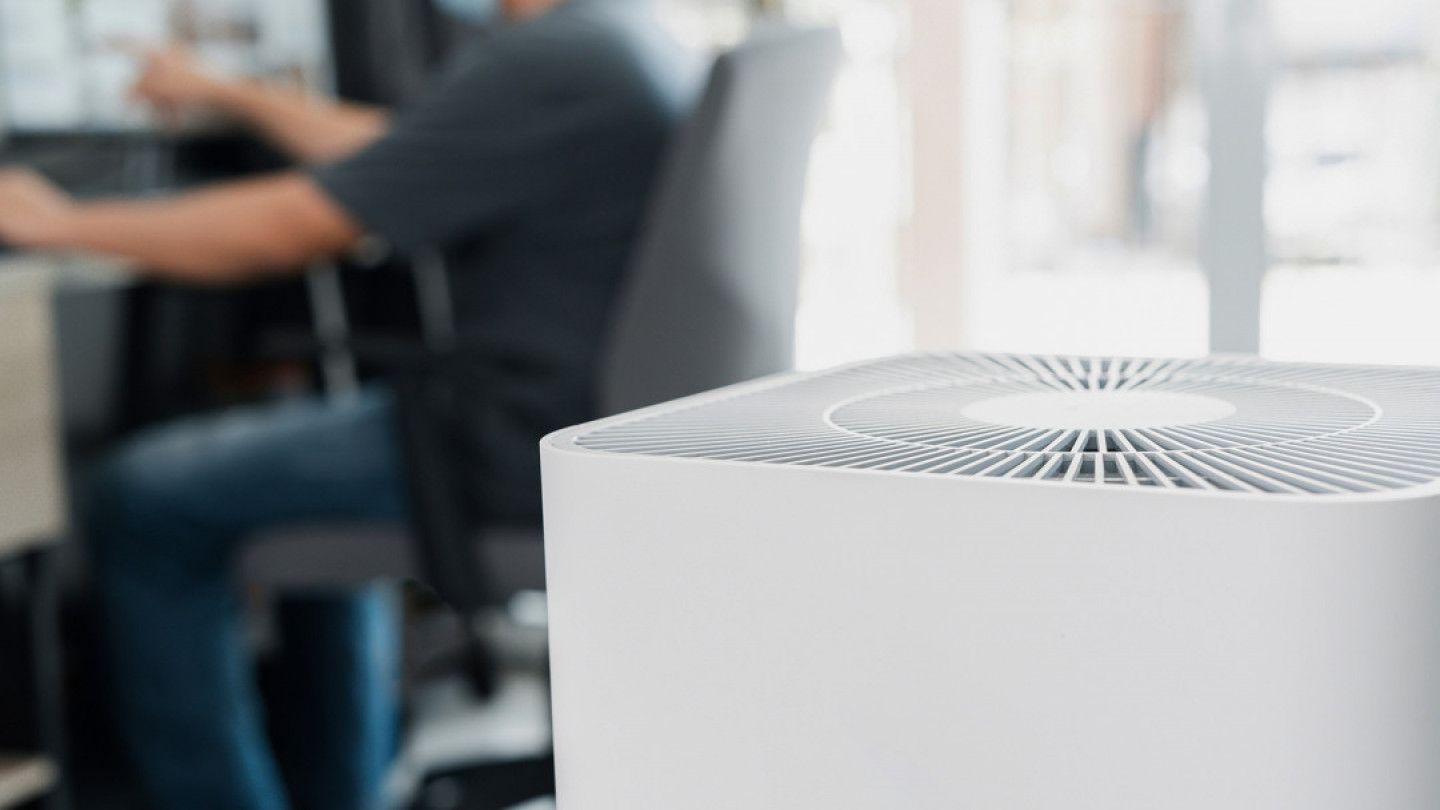 A man is sitting at a desk in front of a air purifier.