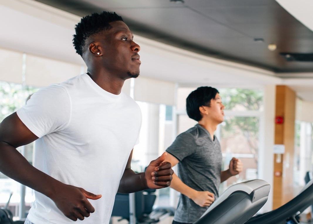 Two men are running on treadmills in a gym.