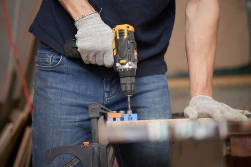 A man is using a drill to drill a hole in a piece of wood.