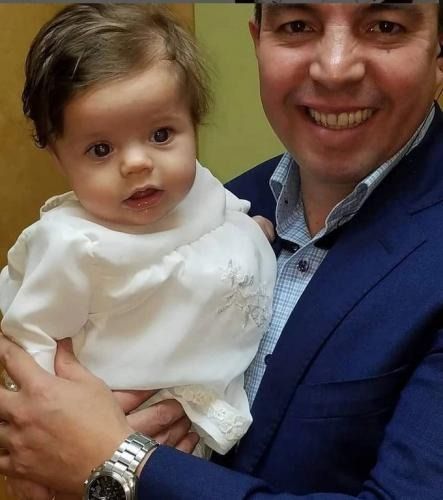 Adult holding a baby, both smiling indoors.