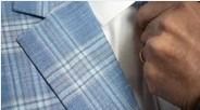 Close-up of a blue plaid suit jacket and a hand adjusting a white shirt collar with tie