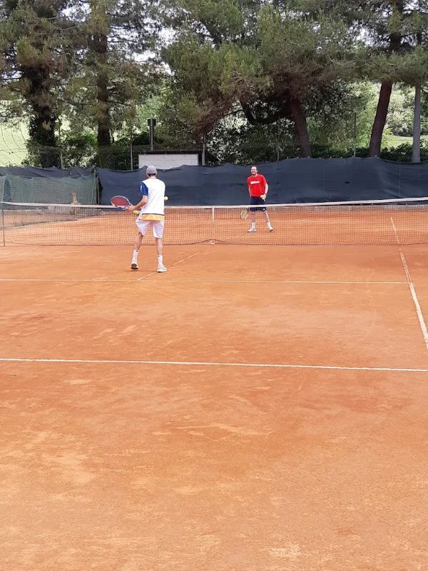Due tennisti su un campo in terra battuta, uno in divisa bianca e l'altro in divisa rossa, si scambiano palla vicino alla rete.