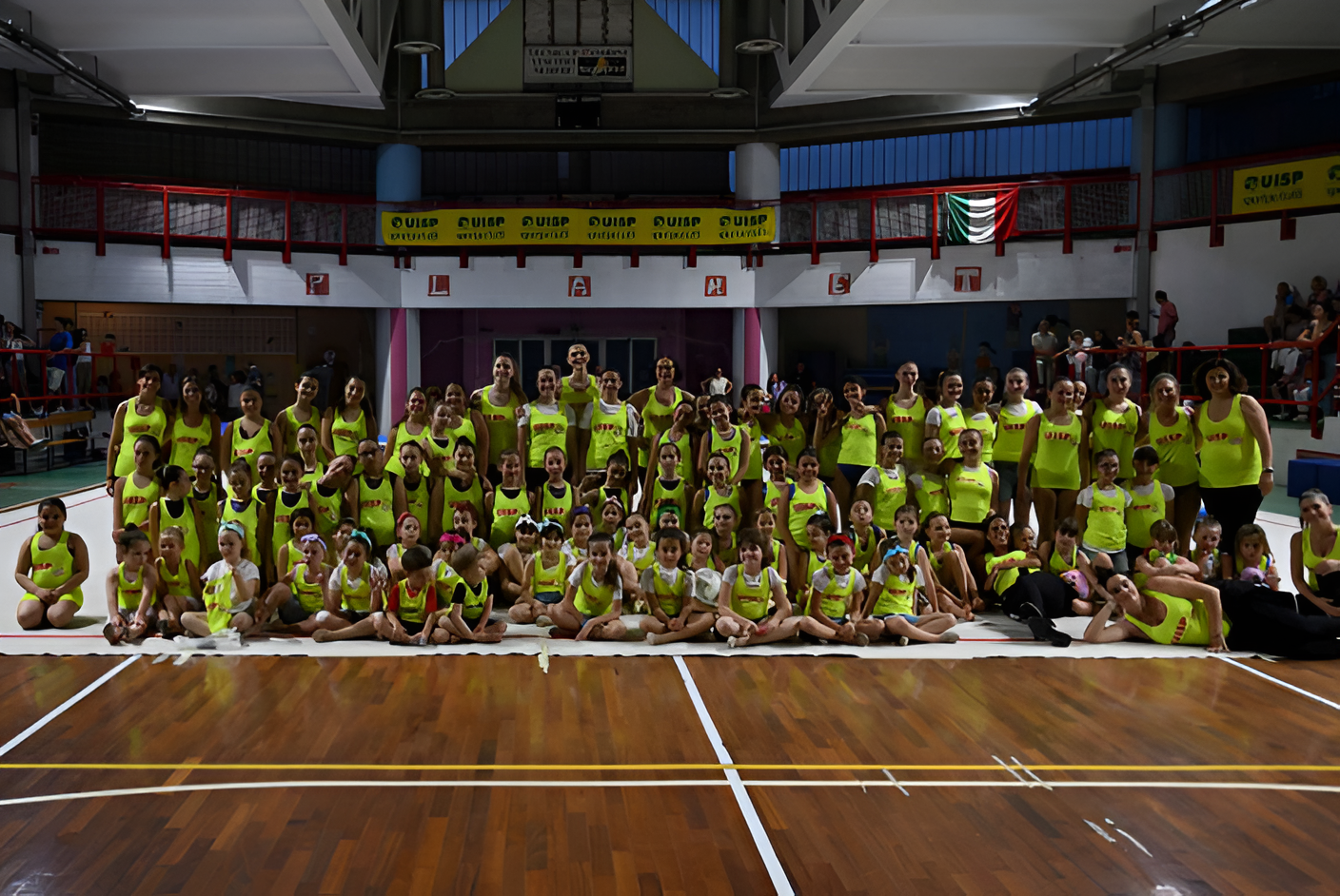 Un folto gruppo di persone con indosso magliette giallo brillante posa su un campo da basket al coperto sotto uno striscione.