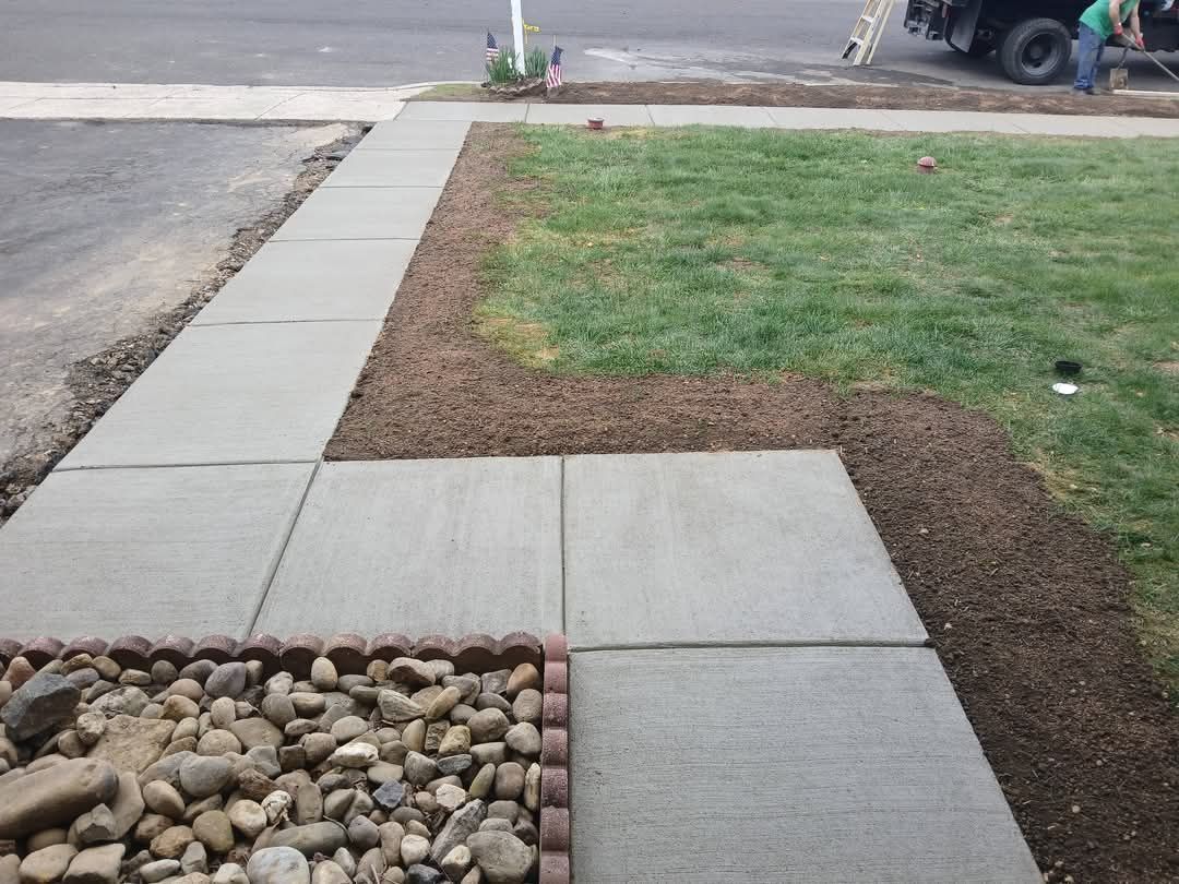 Concrete sidewalk beside a grassy lawn and rock bed at a street corner.