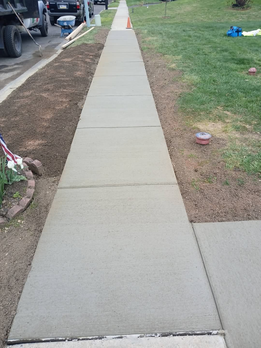 Sidewalk beside a grassy lawn and parked vehicles, with a concrete curb ramp in the foreground.