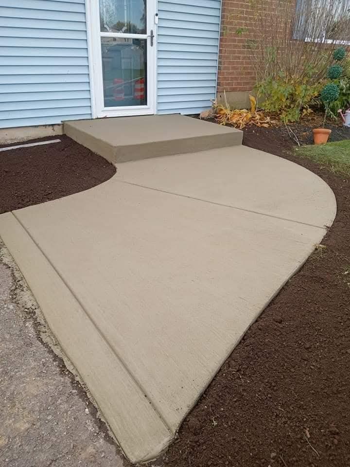 Curved concrete walkway leading to a front door, with adjacent mulch beds and brick siding.