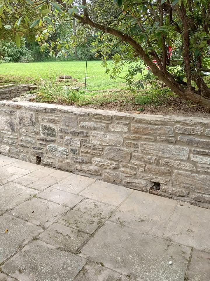 Stone wall beside a paved path, with trees and a grassy park beyond.