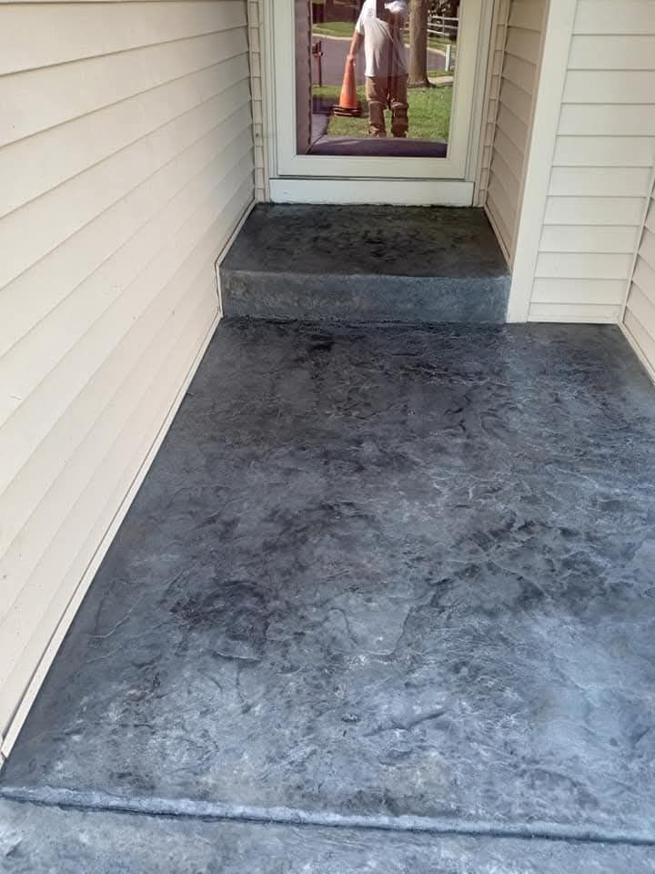 Concrete front porch walkway leading to a doorway, bordered by light siding walls.