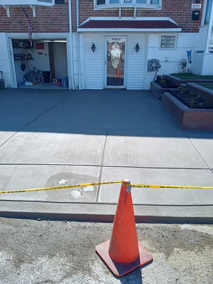 Orange traffic cone on a sidewalk in front of a house with a driveway and garage