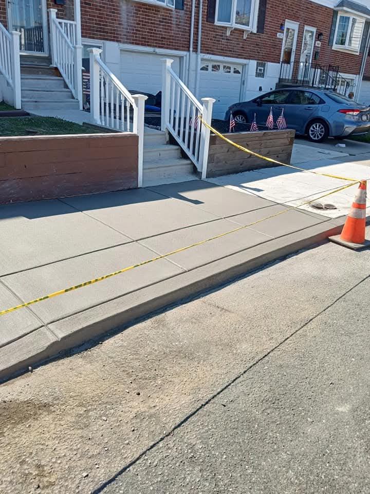 Accessible sidewalk ramp and curb cut beside a brick apartment building, with a parked car and orange cone.