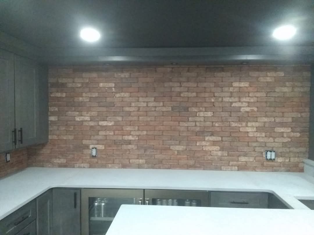 Modern kitchen with dark cabinets, white countertops, and a brick backsplash under recessed lights