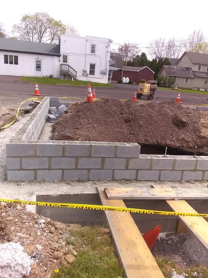 Construction site with unfinished block wall, caution tape, and orange cones in front of houses