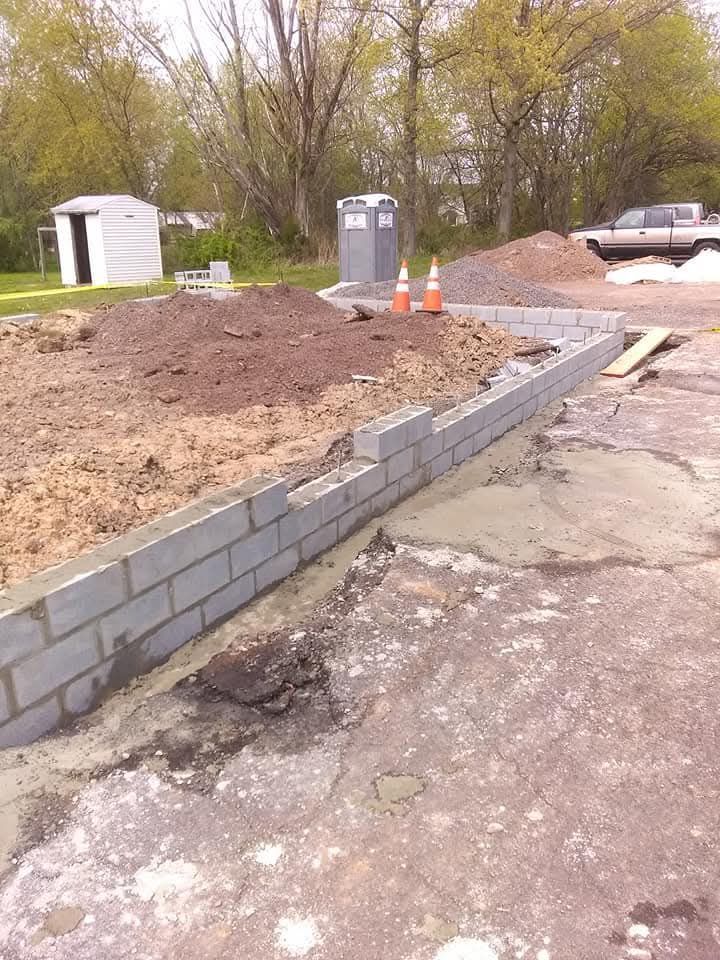 Construction site with a low cinder block retaining wall, dirt piles, and orange traffic cones.