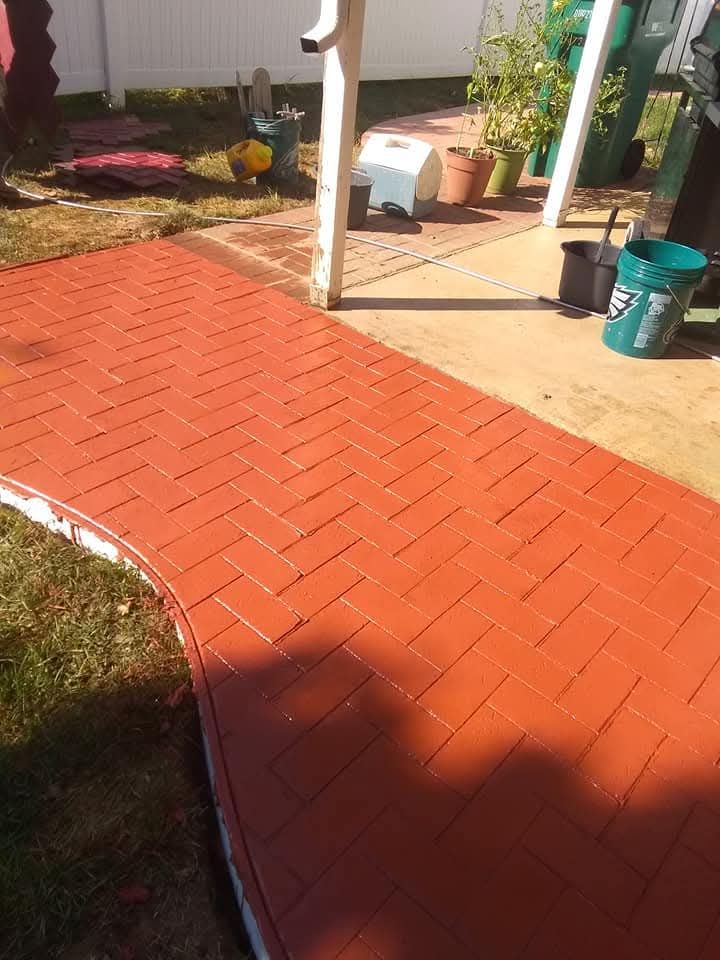 Red herringbone brick pathway curving through a sunny garden patio with potted plants and a green bucket