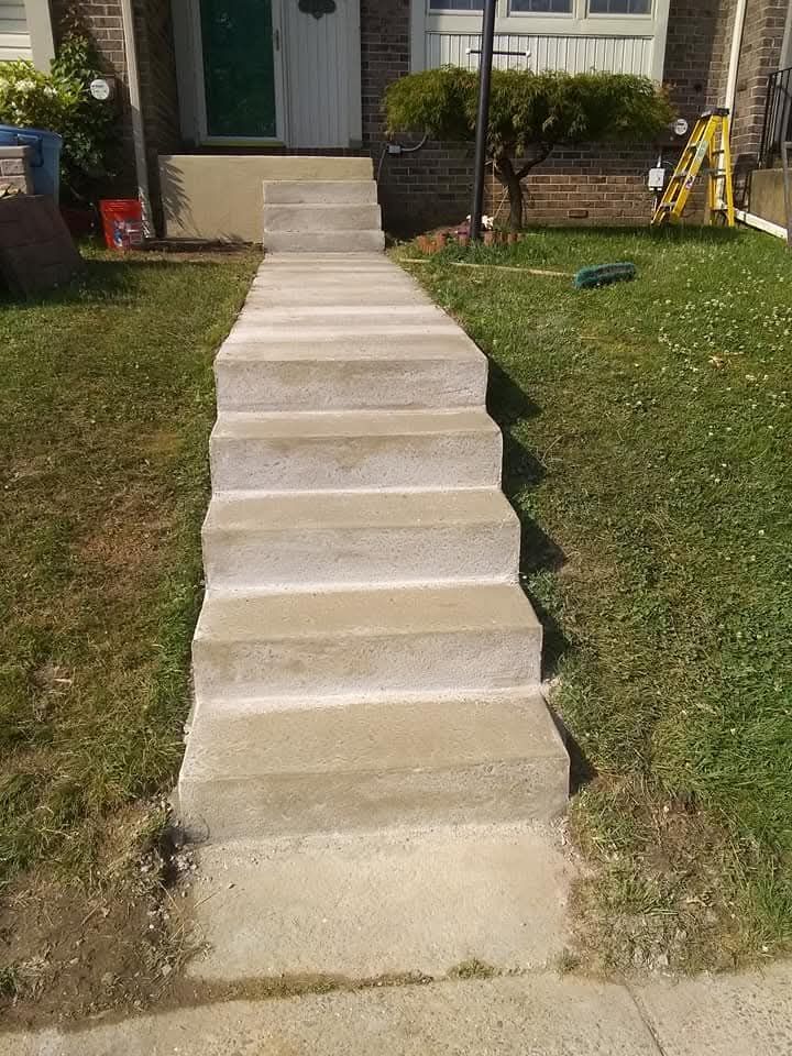 Concrete walkway and steps leading up a house porch, flanked by grassy lawns.