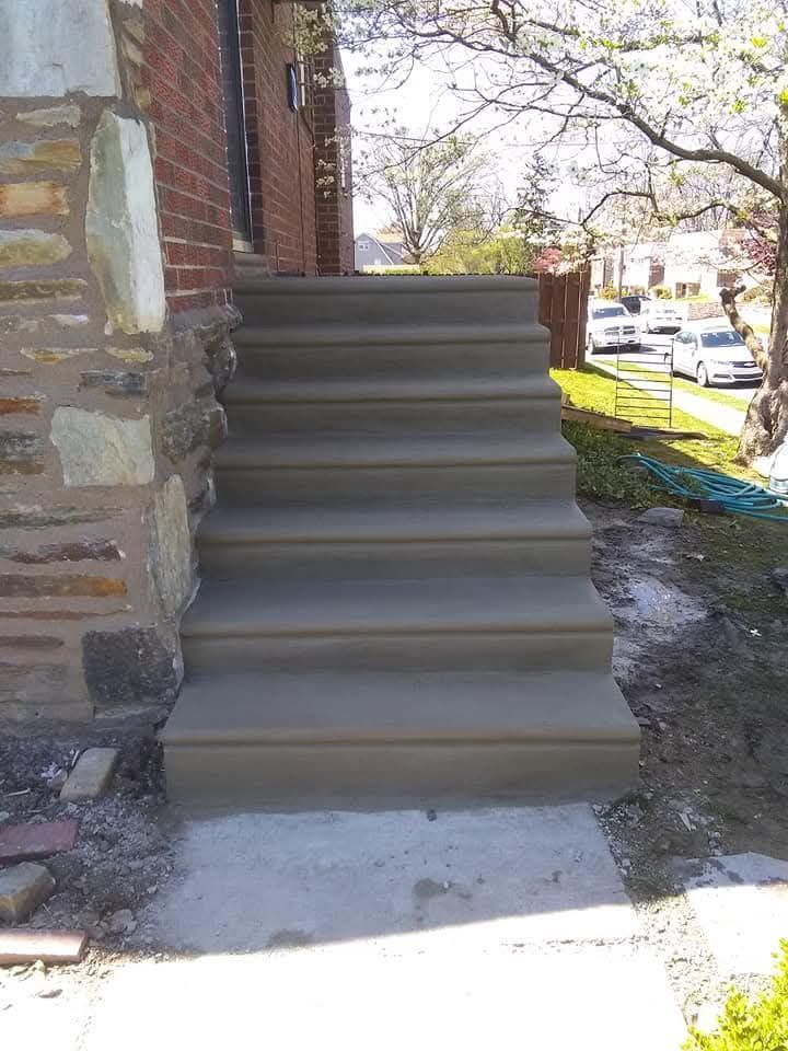 Concrete steps leading to a brick house entrance, with a stone wall and street view beside them