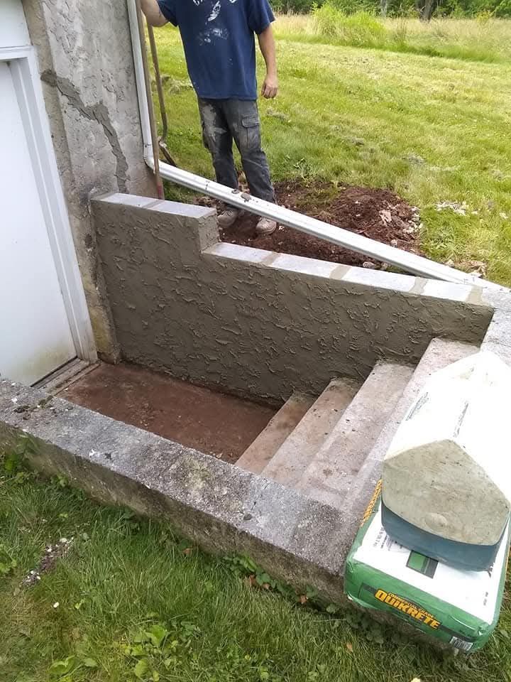 Outdoor basement stairwell with newly built concrete walls and steps beside a house.