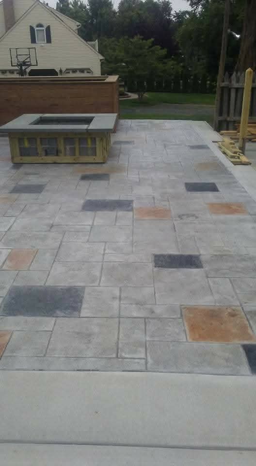 Stone patio with light gray pavers and dark accent tiles beside a house and bench