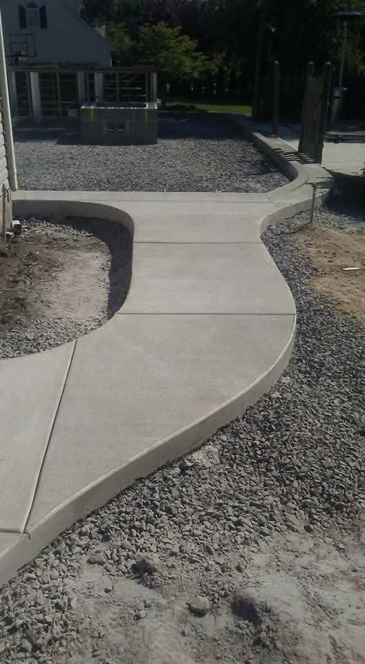 Curved concrete walkway bordered by gravel, leading to a house entrance in a landscaped yard