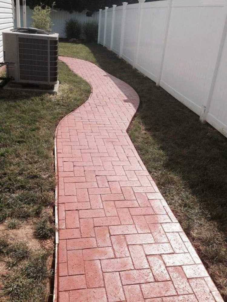 Curving red brick walkway beside a white fence and an outdoor air conditioner unit