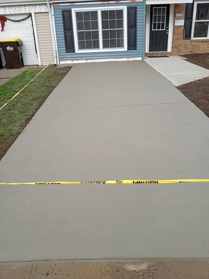 Freshly poured concrete driveway in front of a house, with a yellow caution tape across it.