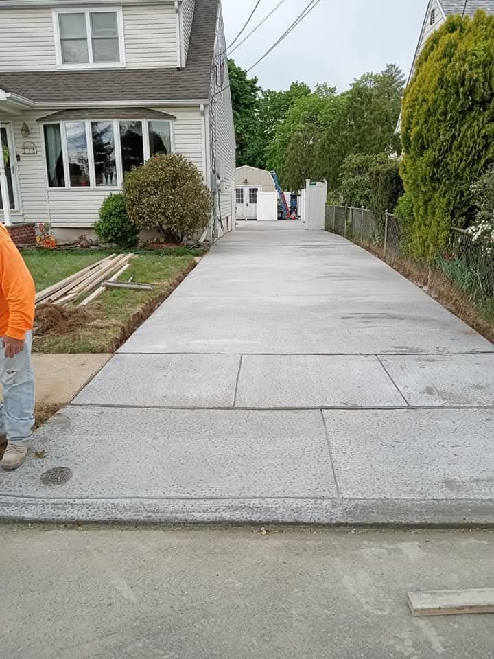 New concrete driveway beside a house, with a narrow path extending to a small white building.