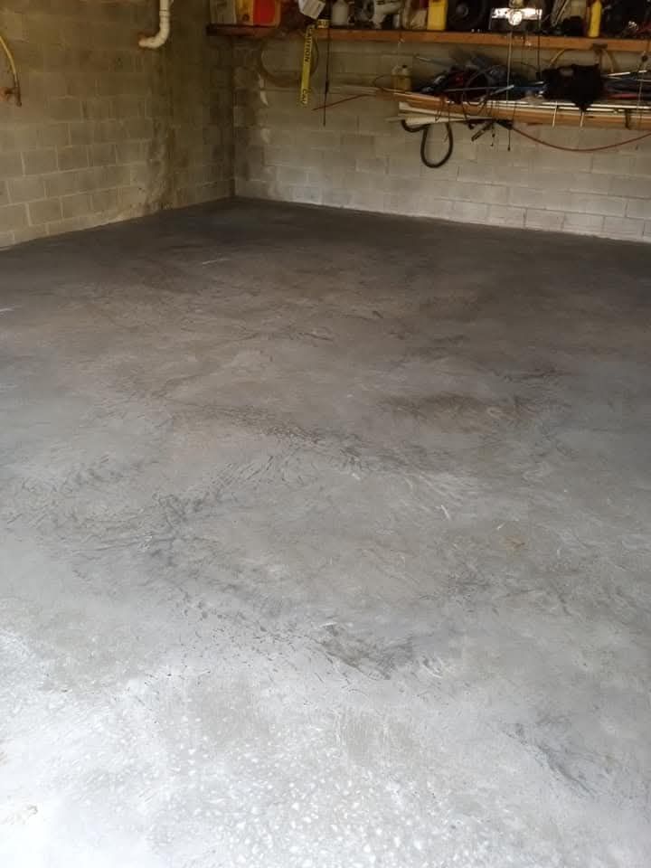 Empty concrete-floored garage with cinderblock walls and a workbench in the back.