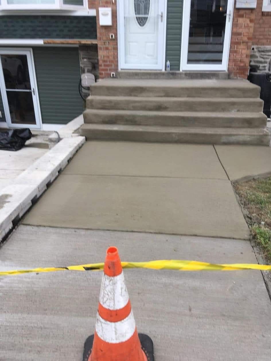 Orange traffic cone blocking a concrete sidewalk in front of house steps