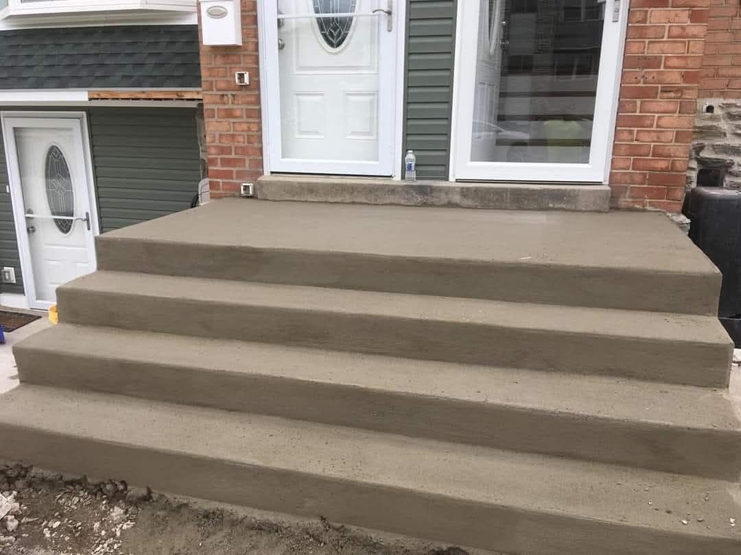Concrete front steps leading to a white door on a brick house