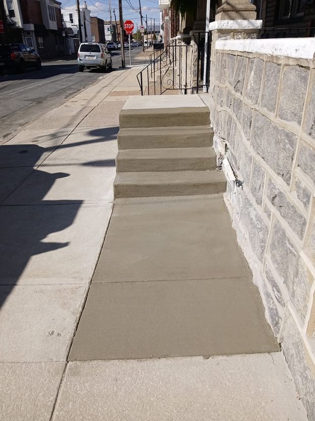Concrete wheelchair ramp beside a stone wall on a city sidewalk