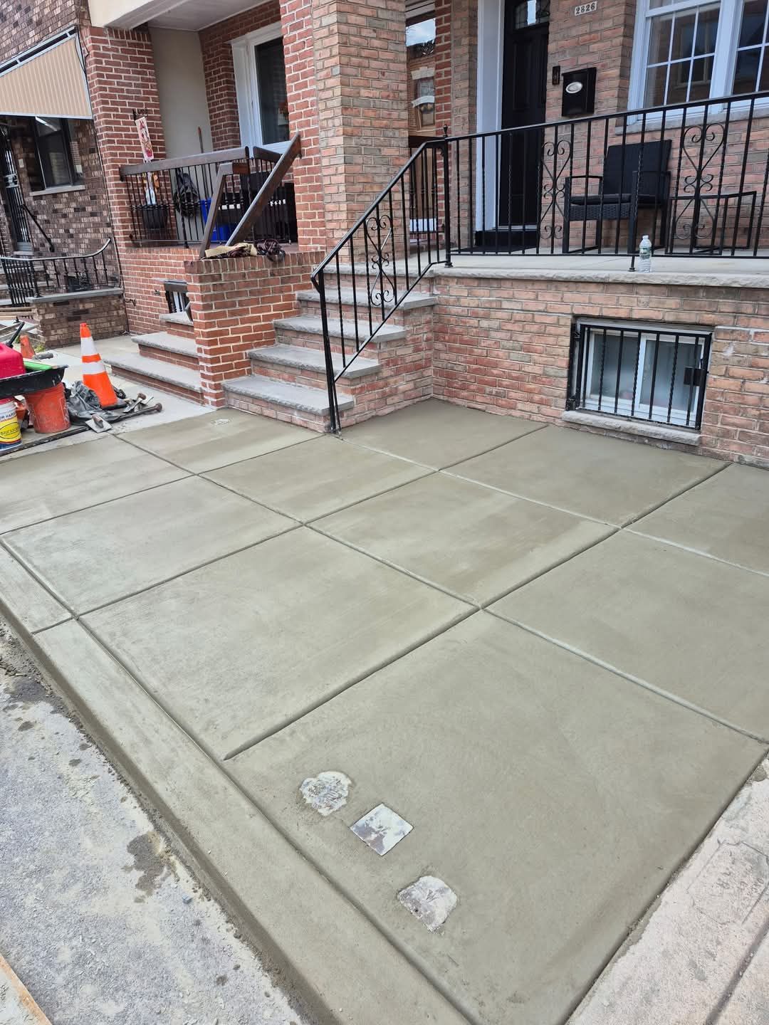 Freshly poured concrete front patio with steps, brick rowhouse, and construction cones nearby