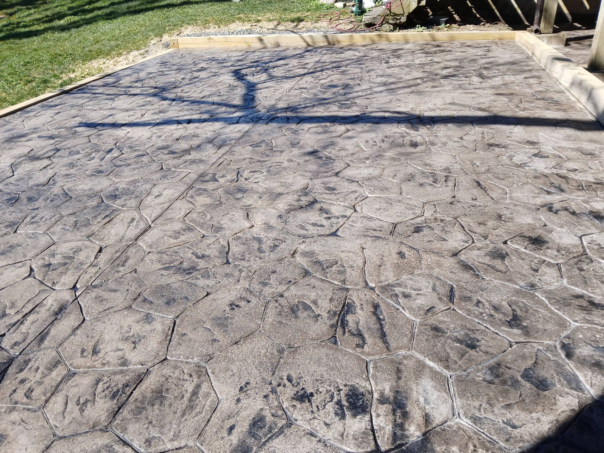 Stamped concrete driveway with leaf shadows and a grassy edge under bright sunlight