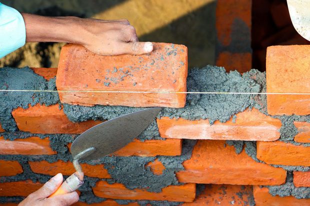 Hands spreading mortar between orange bricks in a masonry wall