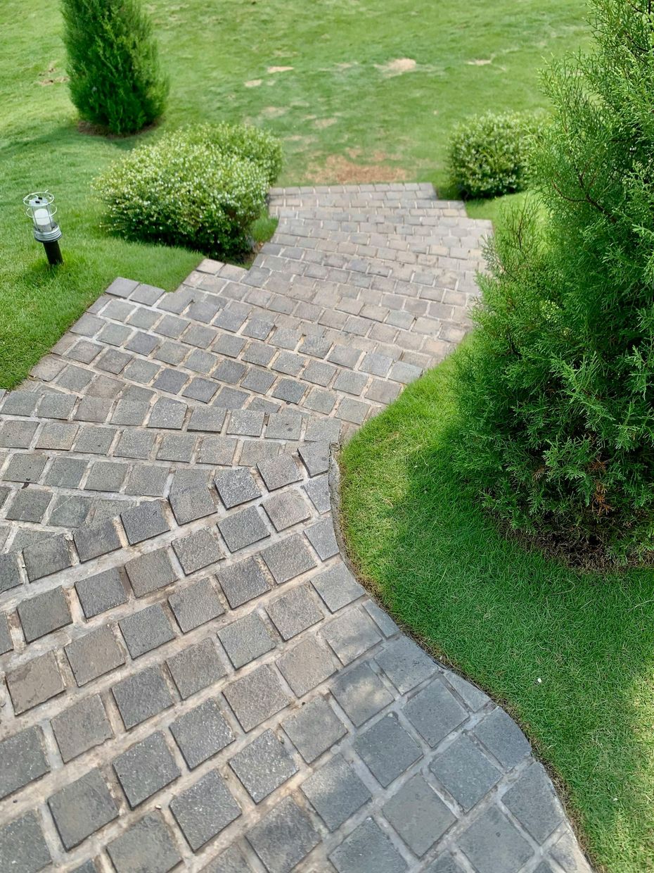 Curved cobblestone garden path bordered by green grass and shrubs