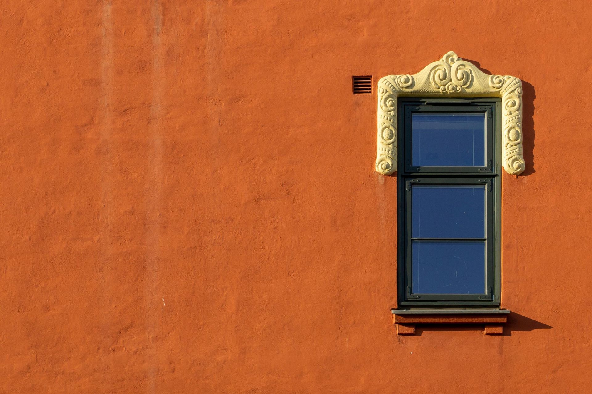 Blue window with ornate trim on an orange stucco wall