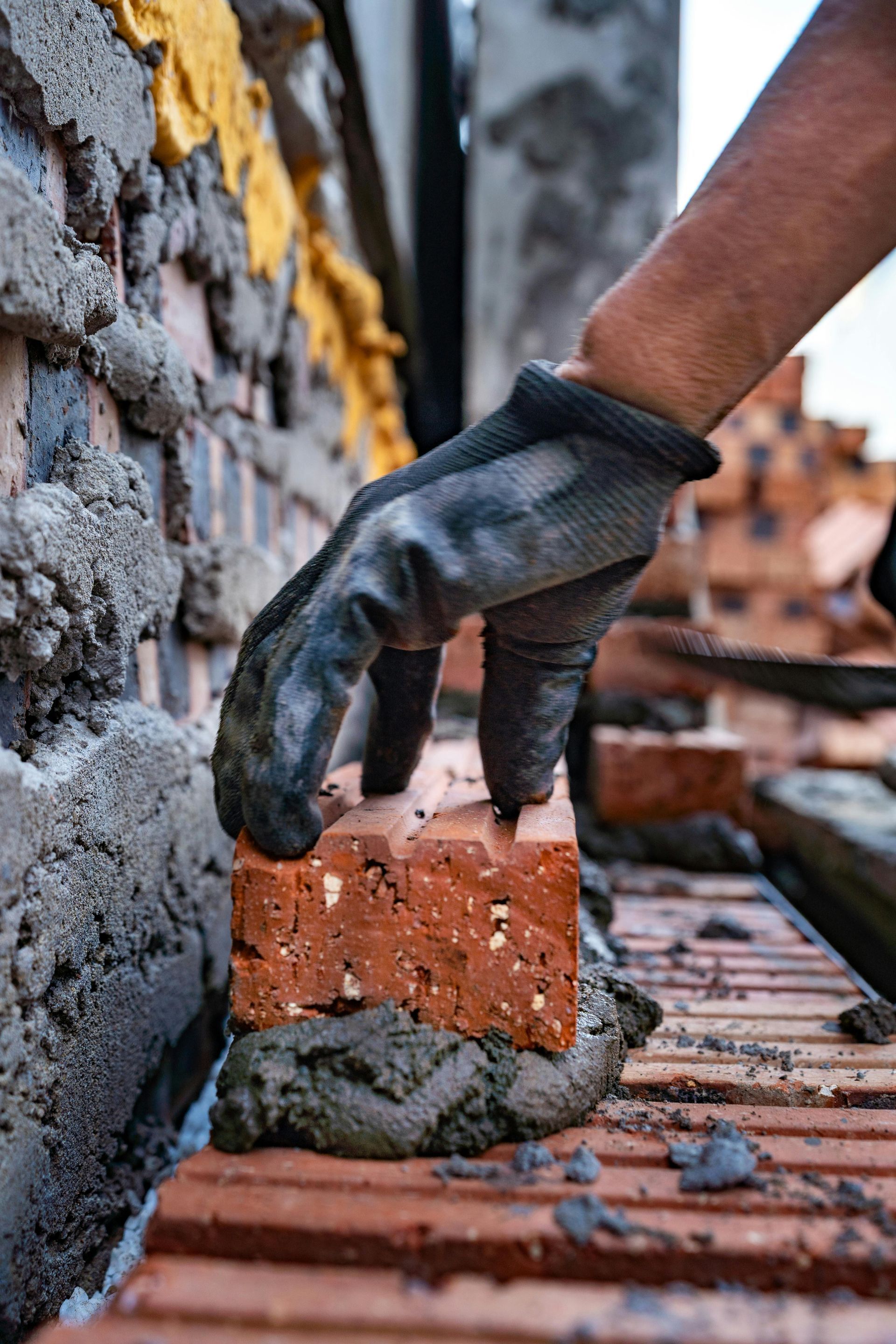 Gloved hand placing a brick in a brick wall under construction