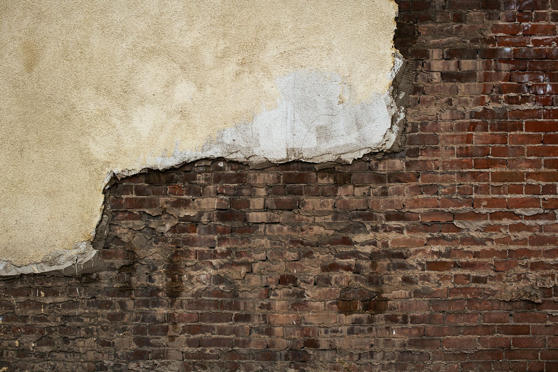 Peeling beige plaster exposing red brick wall and worn masonry