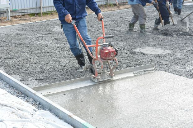 Worker smoothing fresh concrete with a trowel machine on a construction site