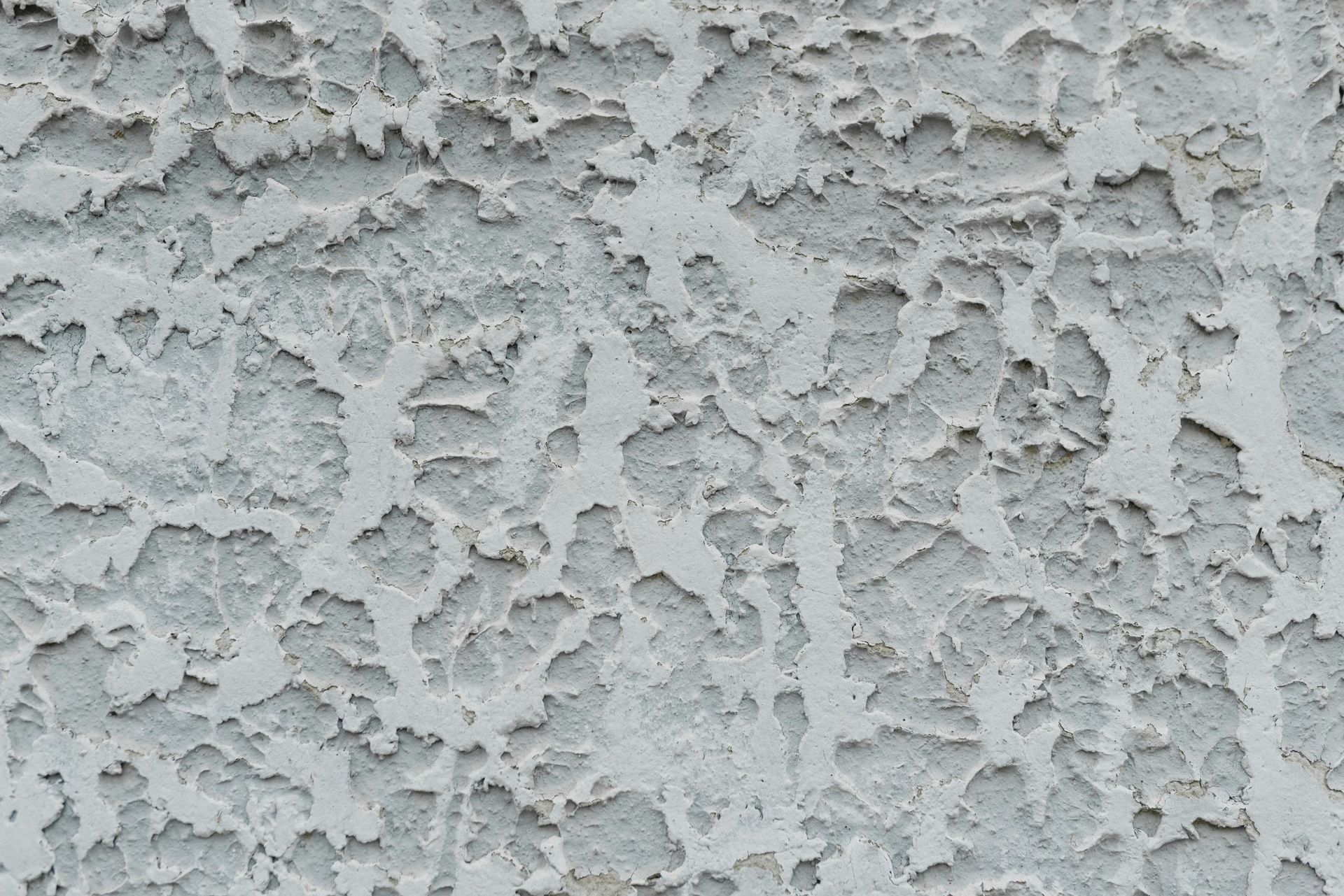 Close-up of gray textured stucco wall with rough, peeling surface