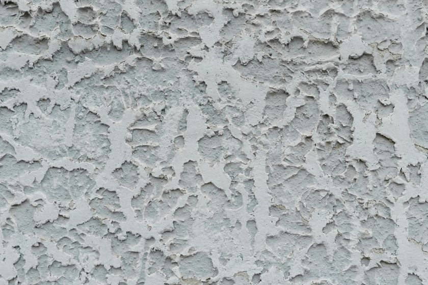 Close-up of gray stucco wall with rough, textured surface and peeling paint.