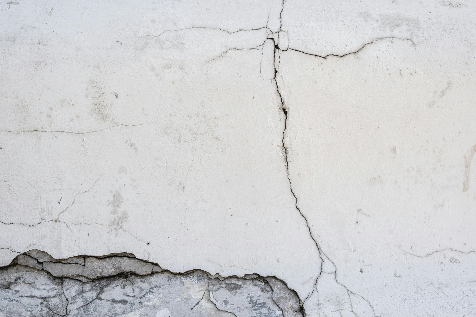Cracked white plaster wall with peeling paint and a horizontal chip along the bottom edge