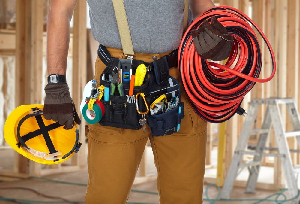 A Man Wearing A Hard Hat And A Tool Belt Is Holding A Coil Of Wires — Barcou Electrics In Gordonvale, QLD