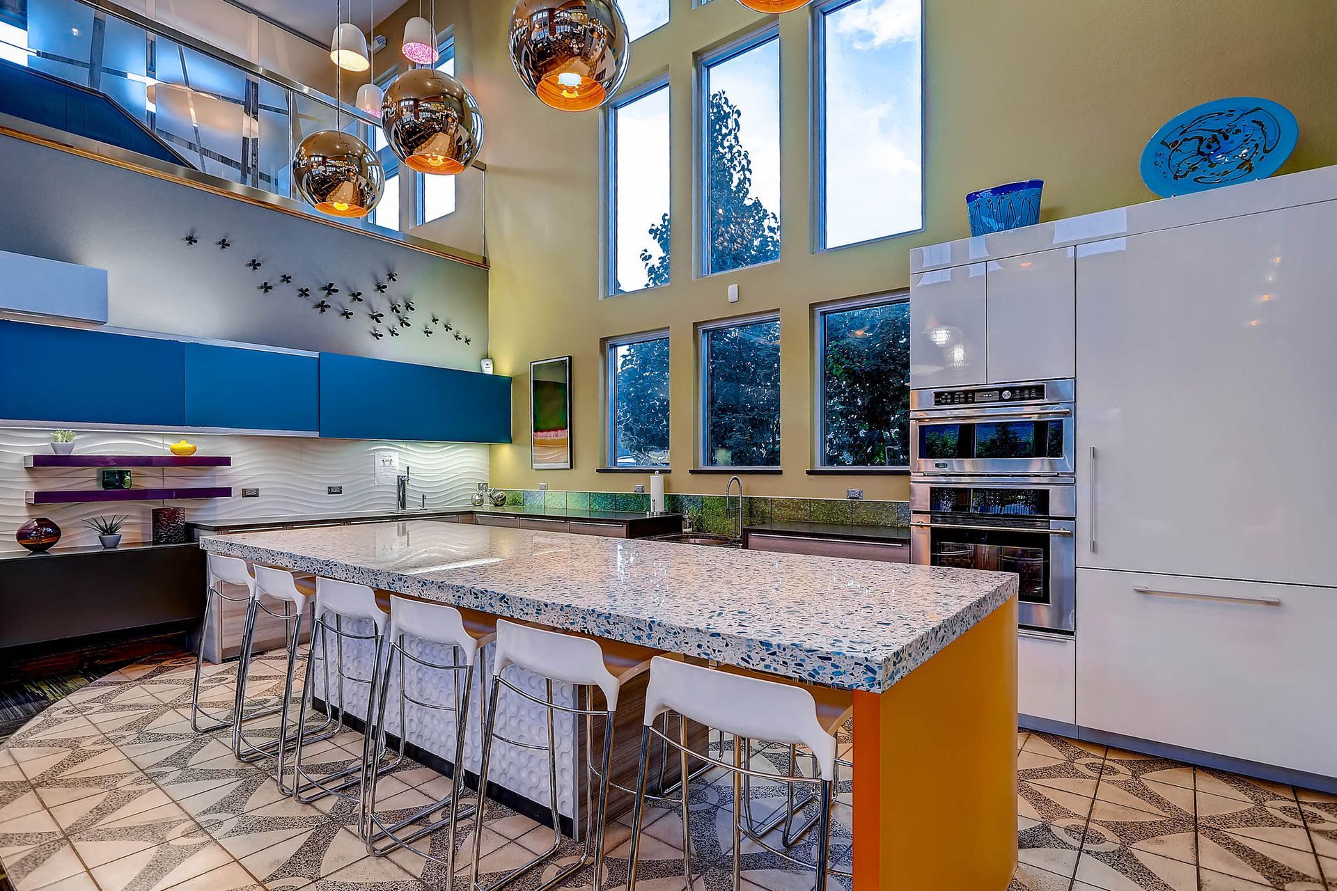 Modern communal kitchen with a large terrazzo island, blue cabinets, and tall windows